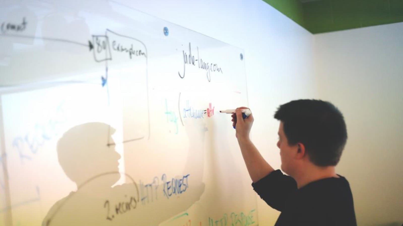 A person writing notes on a glass whiteboard during a planning session