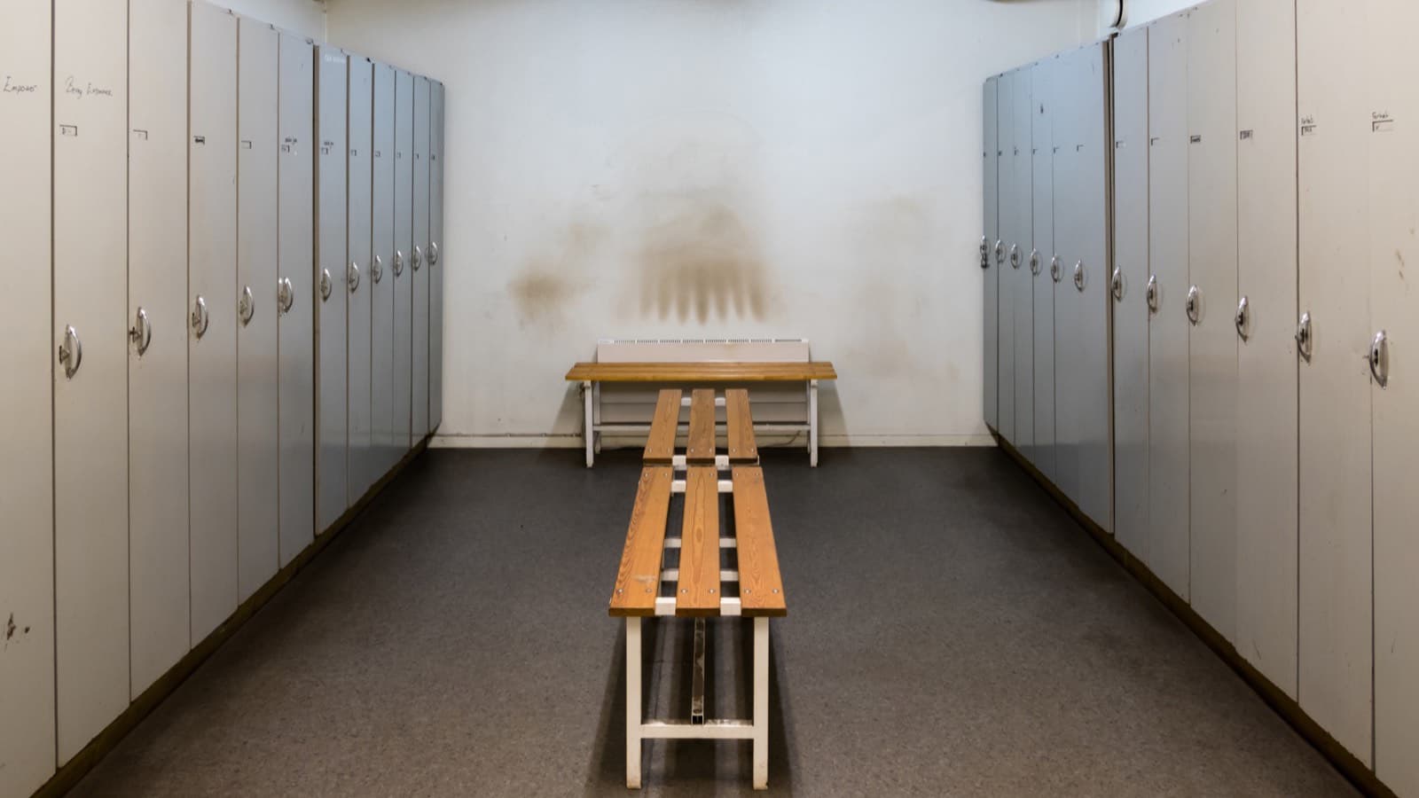 A locker room with two rows of closed lockers and a wooden bench between them
