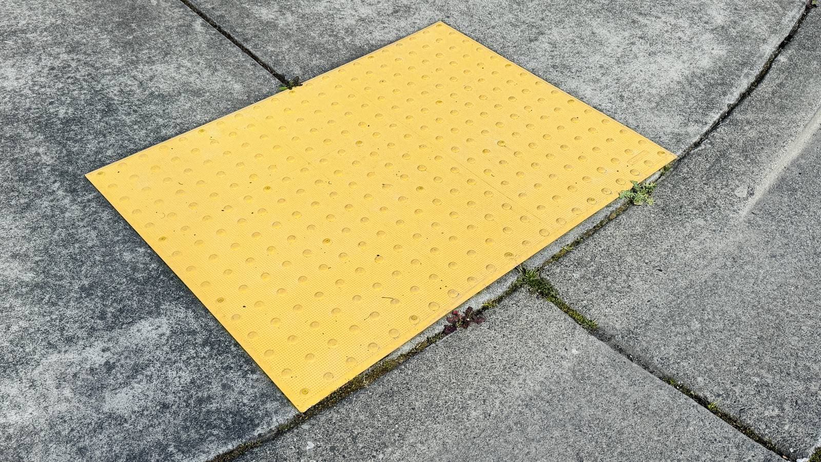 A yellow tactile paving panel set into a grey concrete pavement