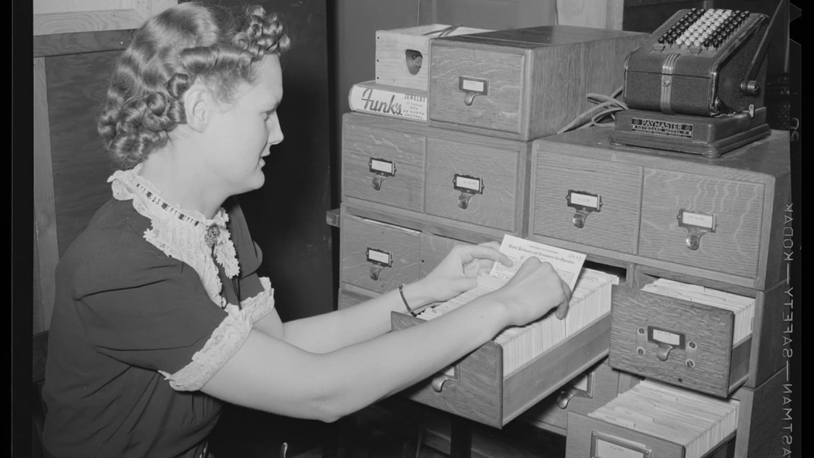 A woman filing a card into a wooden card index cabinet, in black and white