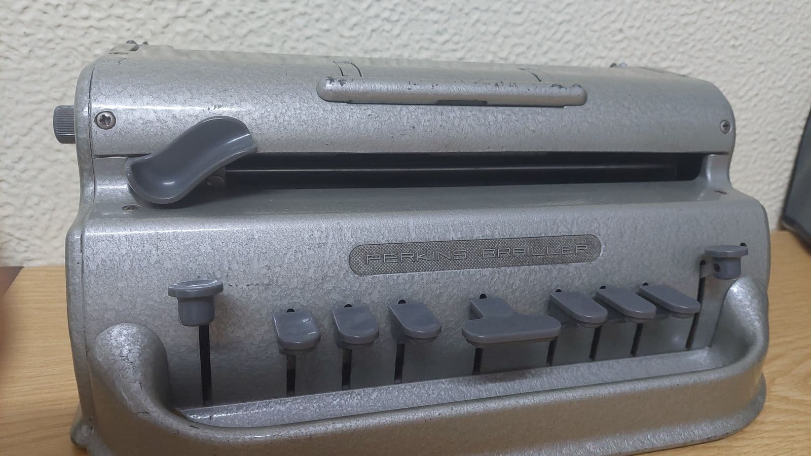 An old grey Perkins Brailler machine standing on a wooden desk