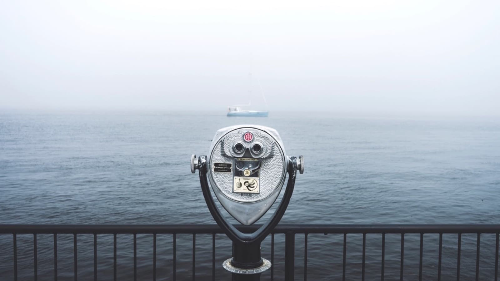 Coin-operated tower viewer binoculars facing a sailboat on a foggy sea