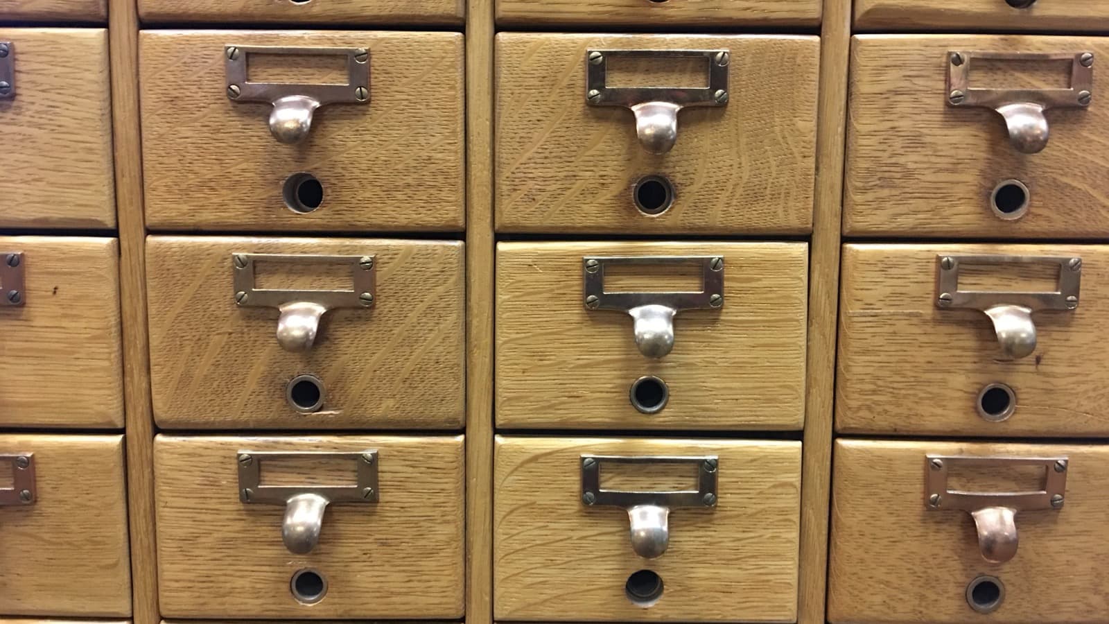 A wall of wooden card-catalog drawers with empty brass label holders
