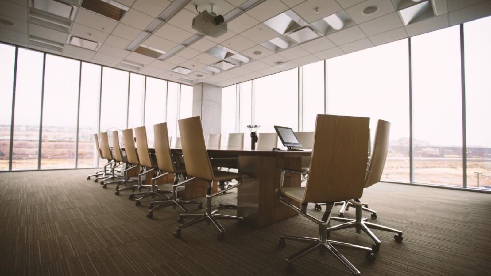 An empty boardroom with a long table and chairs beside tall windows