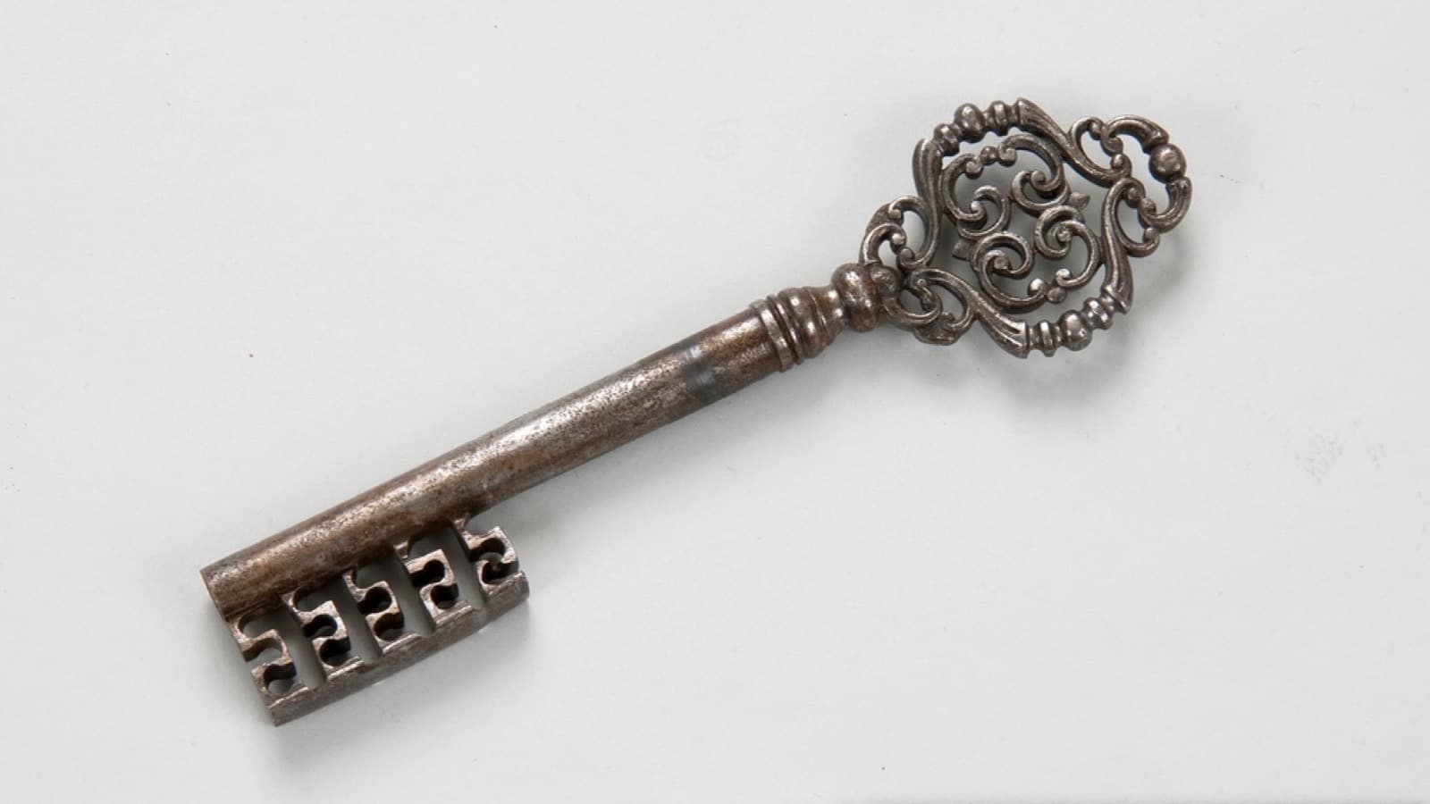 An ornate antique iron key with a pierced bow, photographed on white
