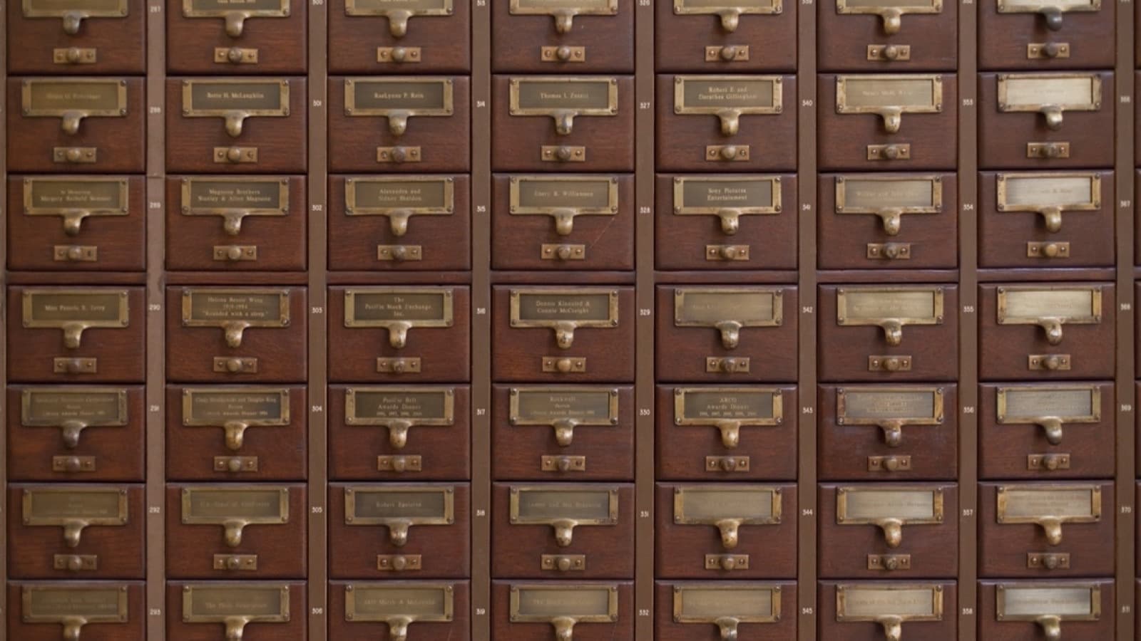 A wall of dark wooden card catalog drawers with brass label holders