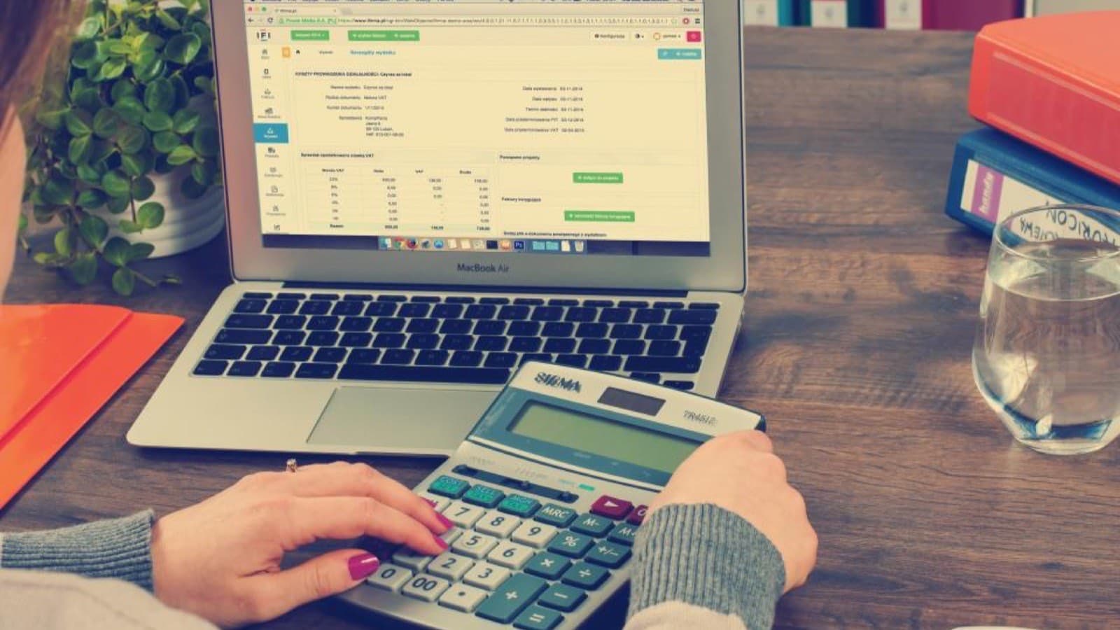 A desk calculator beside a laptop showing a spreadsheet on a wooden desk