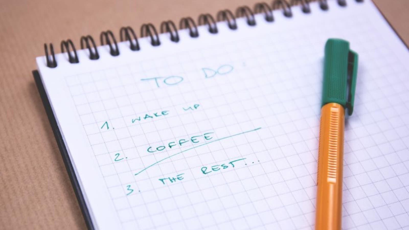 A spiral notepad with a short handwritten to-do list beside a pen