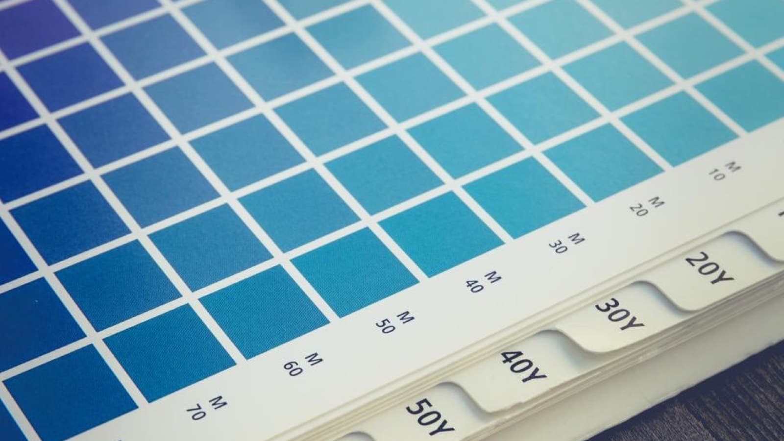 A printer's colour swatch book open on a dark table beside a small loupe