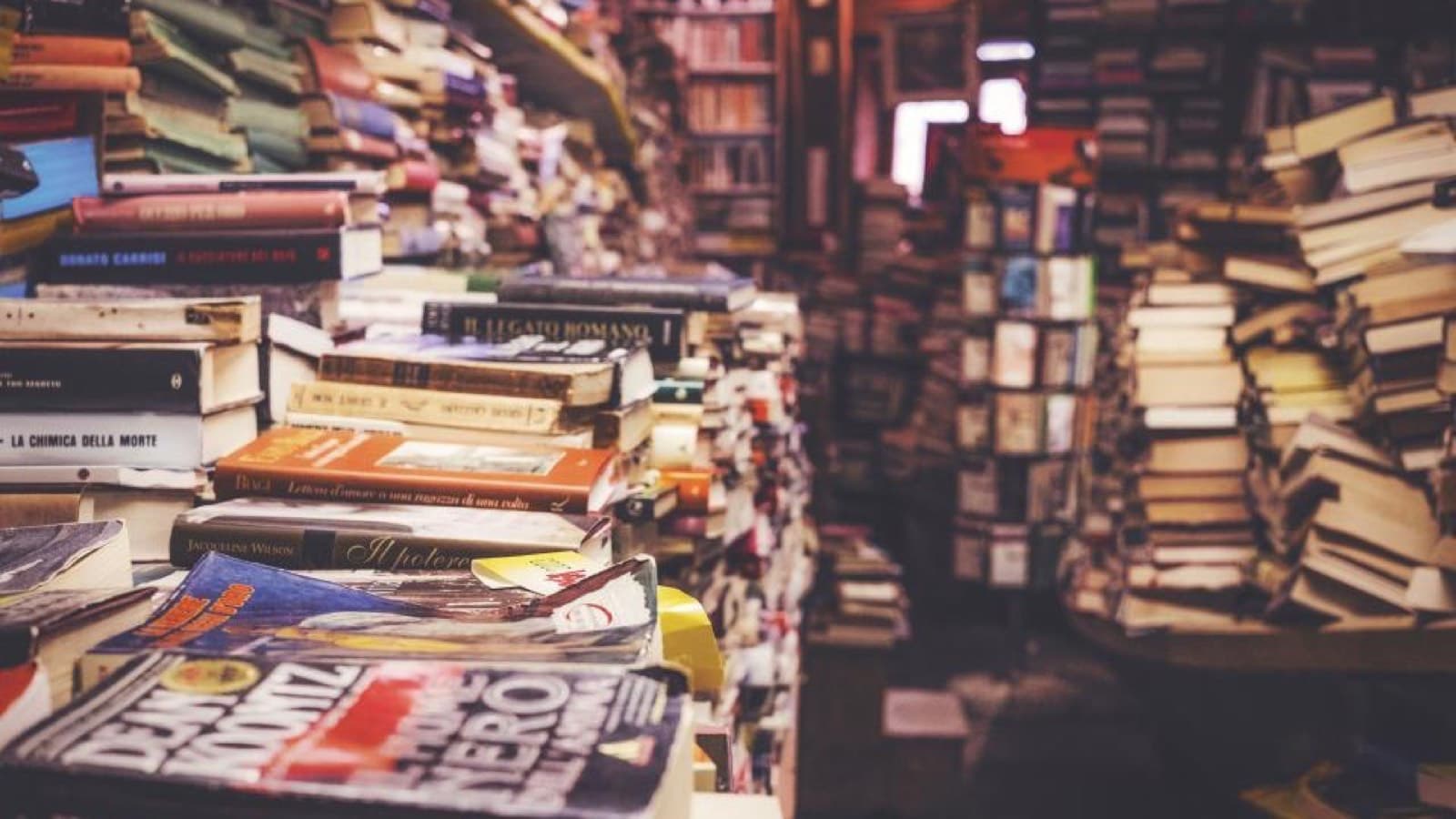 Stacks of secondhand books piled on tables in a crowded bookshop