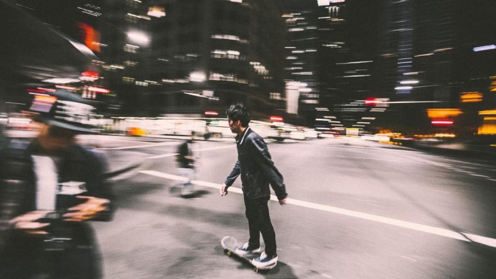 A skateboarder rolling through a city street at night, the lights blurred with motion