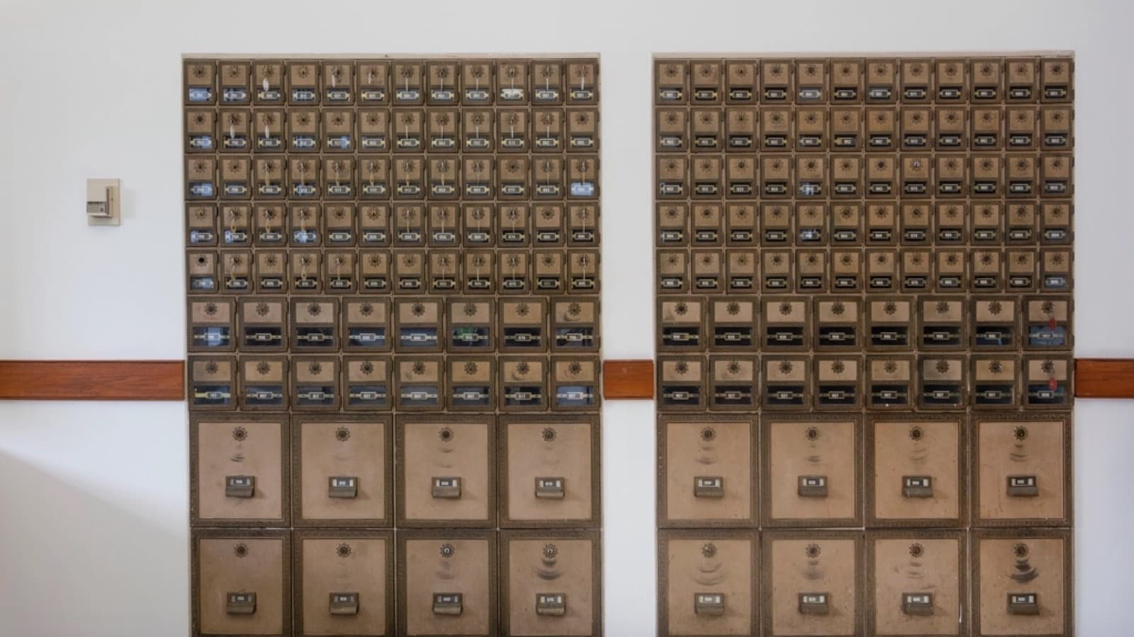 Two banks of brass post office boxes with numbered combination-lock doors