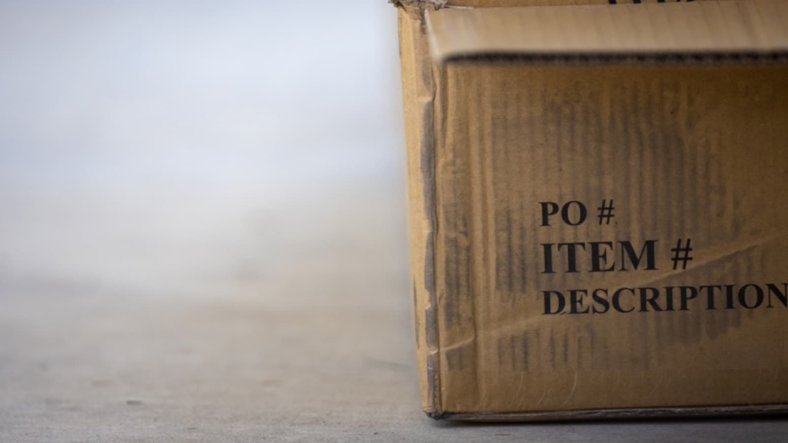 A cardboard shipping box printed with purchase-order fields, standing on a concrete floor
