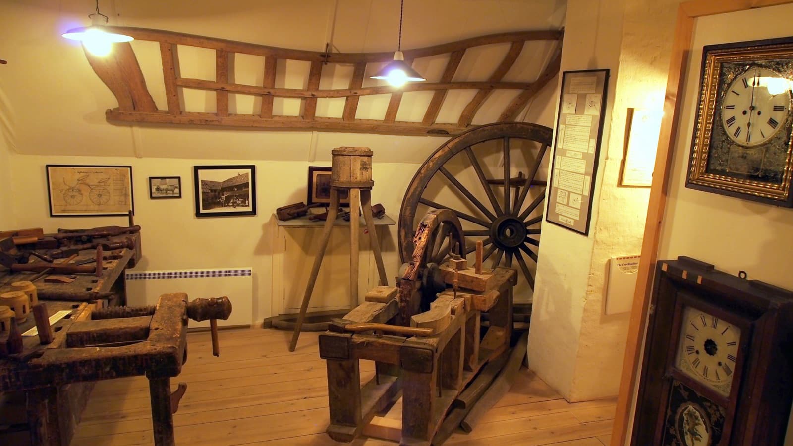 A carpenter's workshop with wooden workbenches, a cartwheel and hand tools under warm lamps