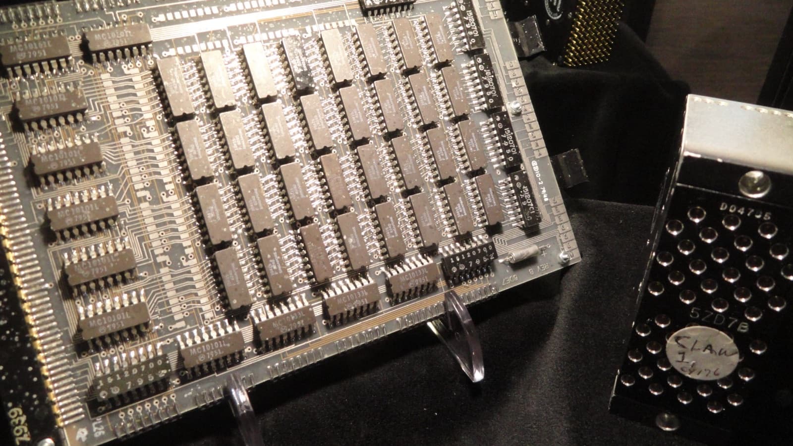 A vintage computer circuit board densely packed with memory chips, displayed on a stand