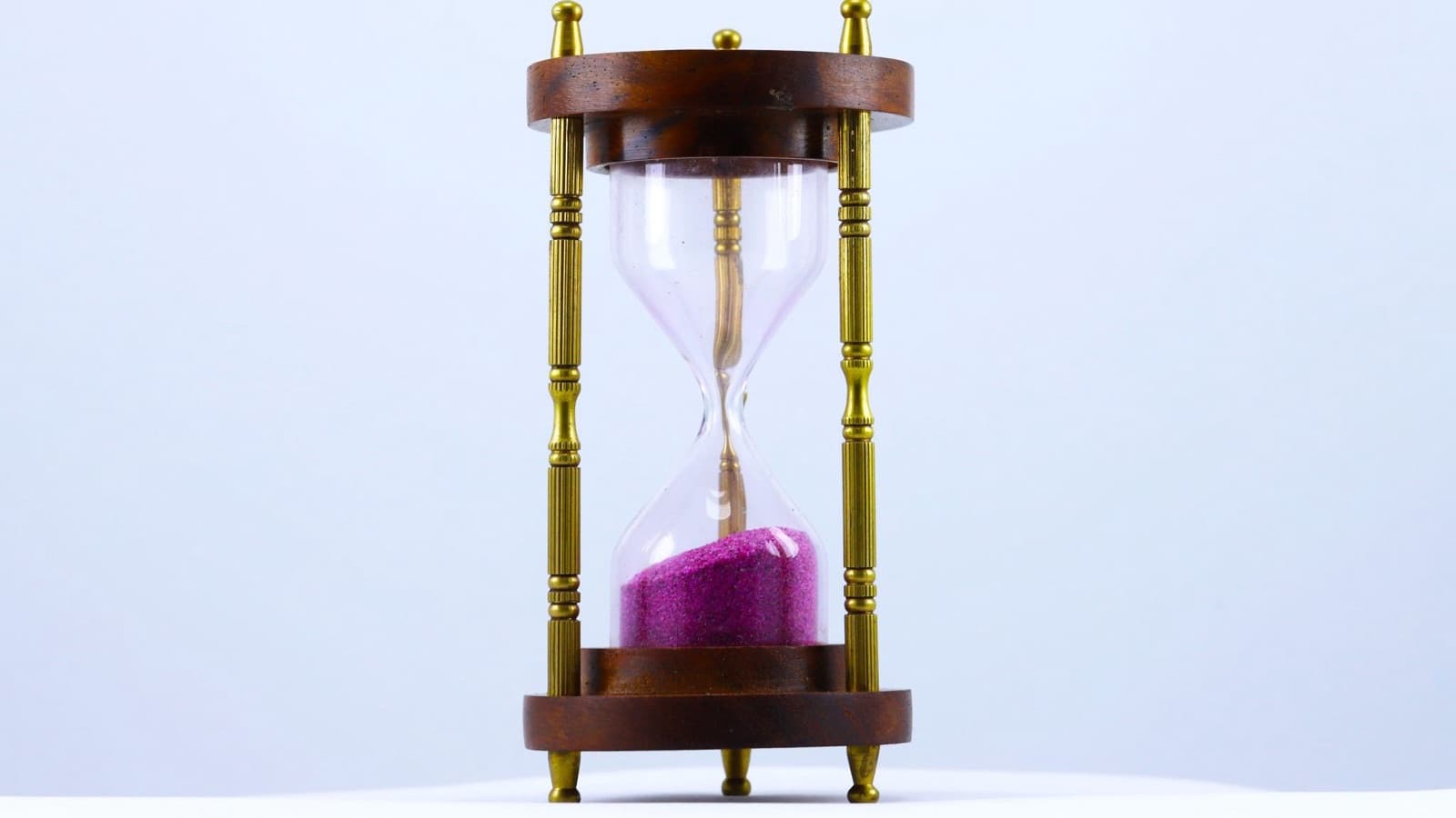 A wooden hourglass with brass columns and purple sand against a pale blue background